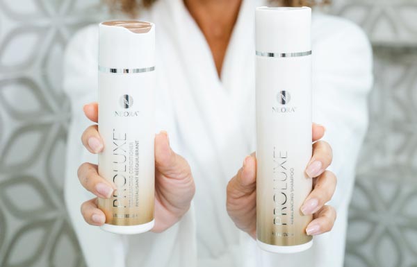 Lifestyle shot of a woman in a white robe holding up the ProLuxe Shampoo and Conditioner combo in her hands.